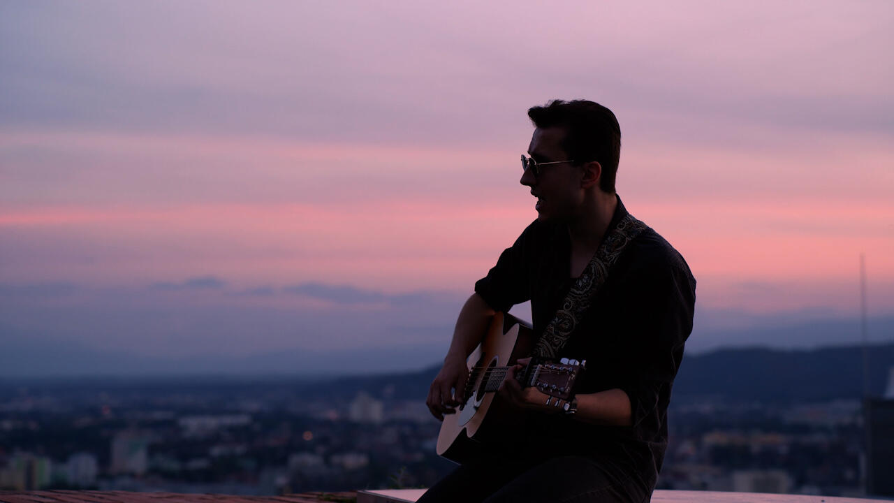 Musiker mit Gitarre, Sonnenuntergang über einer Stadt