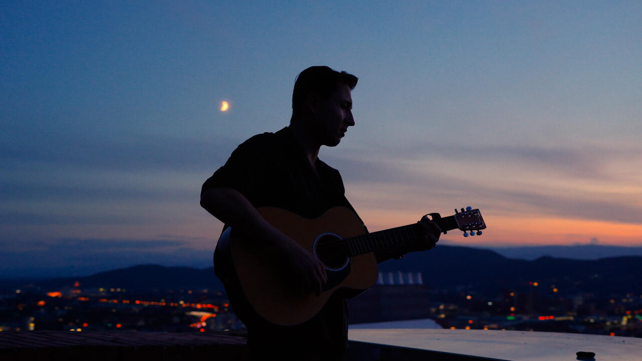 Musiker mit Gitarre, Sonnenuntergang über einer Stadt