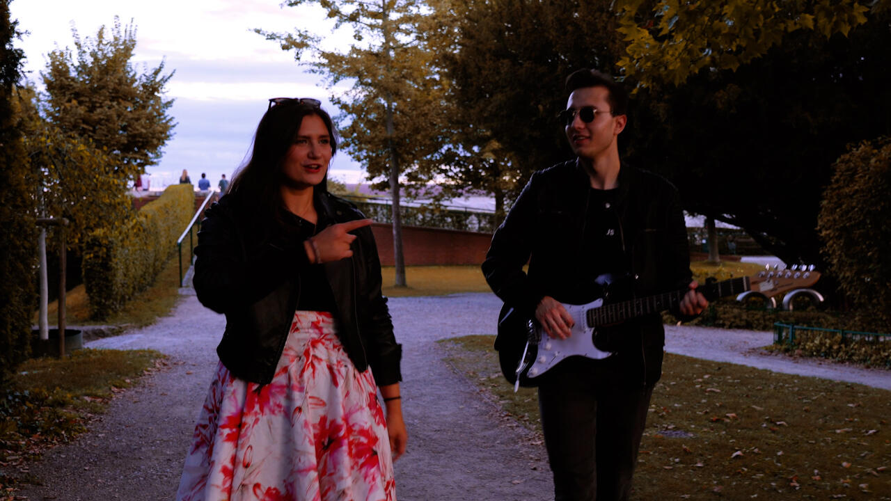 Pärchen geht durch Garten, Musiker spielt währenddessen Gitarre